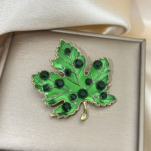 Detailed close-up of maple leaf brooch with green enamel and emerald rhinestones