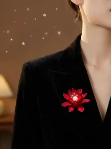 Detail einer roten Lotus-Brosche mit weißer Perle auf einem schwarzen Samtrevers