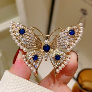 Elegant gold butterfly brooch featuring dark blue main stones and white crystal accents