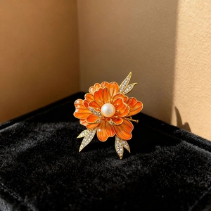 Macro detail of enamel peony brooch with orange gradient petals and a pearl center