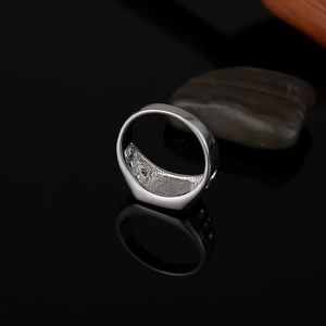 Detailed view of silver signet ring with textured inner band on a dark reflective surface