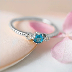 Silver ring with round blue gemstone and embossed dot band on a floral background