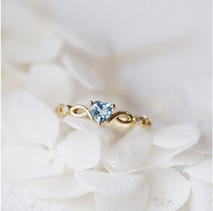 Elegante anello d'oro con cuore di topazio blu tra petali di fiori bianchi