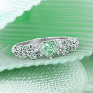 Anello in argento con pietra verde a forma di cuore e accenti di foglie su tessuto verde