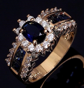 Dettaglio macro dell'anello in oro 18K con zaffiro blu ovale, halo di diamanti e marchio 18K