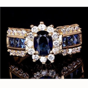Anello di lusso dorato con gemma ovale blu circondata da brillanti diamanti e riflessi nitidi