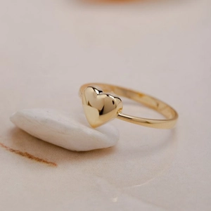 Anillo de corazón dorado minimalista con acabado pulido sobre una piedra natural blanca