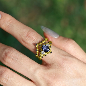 Anello dorato a vite con zaffiro blu ovale e dettagli in diamante indossato sulla mano