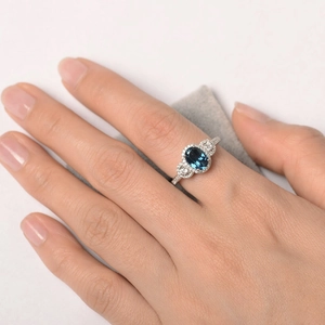 Elegante anello vintage con gemma blu ovale e alone di diamanti su fascia d'argento
