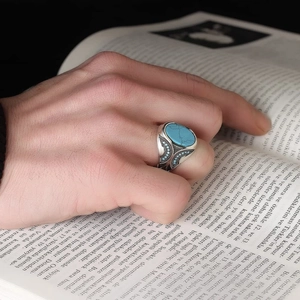 Vintage silver turquoise ring with ethnic hollow patterns on hand over open book