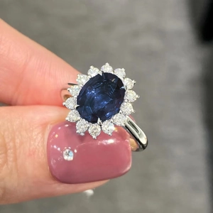 Vista macro di un anello con zaffiro blu ovale e un alone di zirconi bianchi placcati platino