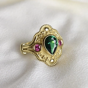 Bague vintage dorée avec gemme verte en goutte et pierres roses sur tissu blanc