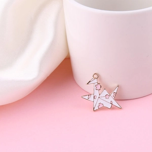 Macro detail of pink and white origami crane enamel pendant with gold metal edges