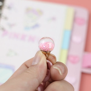 Handheld view of a clear glass ball charm with pink stars and golden cap for DIY jewelry