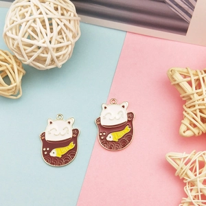 Détail de deux breloques chat porte-bonheur en émail avec bordures en métal doré