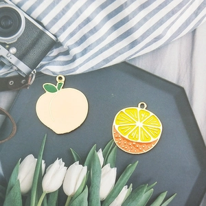 Charming enamel peach and lemon fruit charms on black display tray with floral background