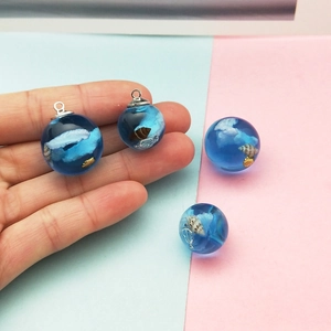 Blauer Glaskugel-Anhänger mit weißen Wolken und Muscheln auf pastellfarbenem Grund