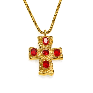 Détail macro du pendentif croix dorée à texture martelée et cinq pierres de zircon rouge