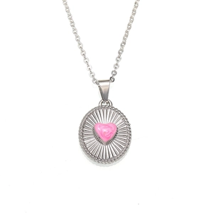 Macro shot of silver oval pendant with pink heart and textured sunburst engraving