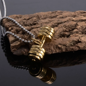 Detailed view of a golden dumbbell pendant on a silver ball chain over a black mirror