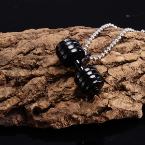 Detail of a black fitness dumbbell pendant on a steel ball chain over tree bark