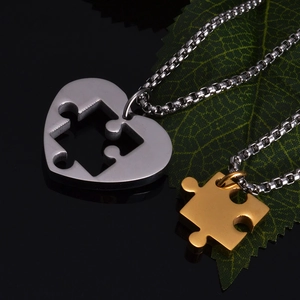 Macro shot of silver and gold heart puzzle necklaces on dark background with green leaf