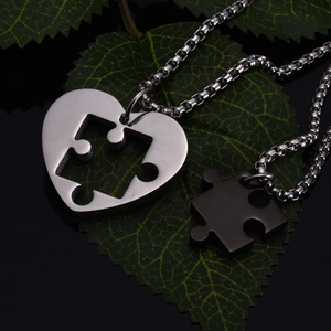 Close-up of puzzle heart couple necklaces in silver and black steel on a green leaf