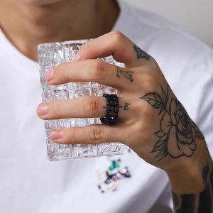 Close-up of a matte black bicycle chain ring worn by a male model holding a glass