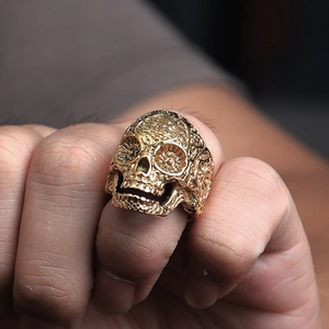 Dettaglio dell'anello a teschio dorato con rilievo totemico sulla mano di un uomo