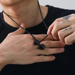 Detail shot of a black matte dumbbell pendant necklace worn by a male model for fitness style