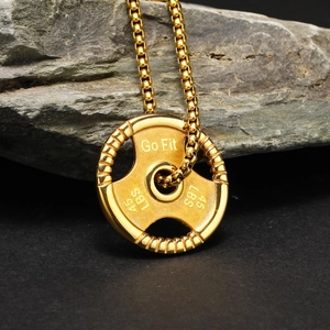 Macro view of golden barbell weight plate pendant engraved with Go Fit on grey stone