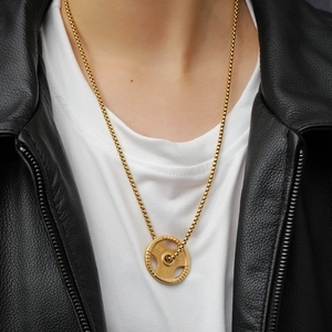 Close-up of golden dumbbell weight plate pendant on box chain worn by male model