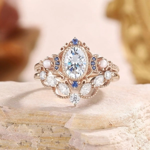 Macro di anelli in oro rosa con pietra bianca ovale e dettagli in diamanti blu scintillanti