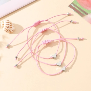 Détail de trois bracelets rose tressés avec breloque cœur et cordon ajustable