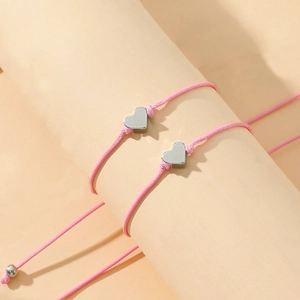 Gros plan des bracelets cœurs tissés roses avec pendentifs argentés sur un support neutre