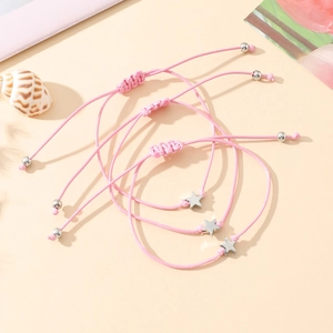 Close-up of three pink braided star charm friendship bracelets on a warm-toned background