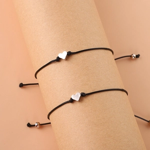 Détail de deux bracelets en cordon noir réglables avec breloques cœur argentées sur support