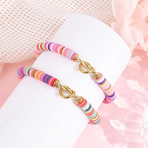 Detail van kleurrijke heishi-kralenarmbanden met gouden hartknoop op roze display