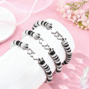 Détail de trois bracelets faits main en perles heishi noires et blanches avec cœurs argentés