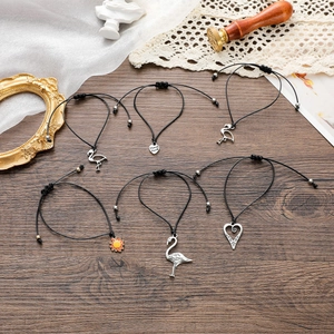Dettaglio di bracciali regolabili in corda nera con ciondoli a forma di fenicottero e cuore