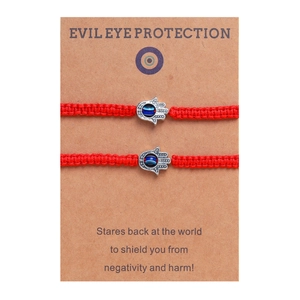Détail de bracelets Hamsa tressés rouges avec breloques œil bleu sur carte