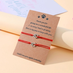 Macro detail of red woven friendship bracelets with silver paw print charms on card
