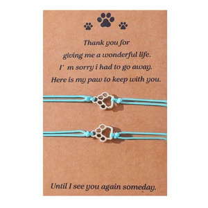 Detailed view of handmade light blue cord bracelets with silver paw charms on a kraft card