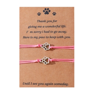 Close-up of pink braided pet memorial bracelets with silver paw heart charms on a card