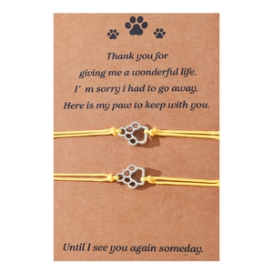 Close-up of handmade yellow string bracelets with silver paw print charms on display card