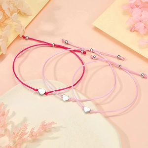 Detailansicht rosa gewebter Armbänder mit Herzanhängern auf weißem Steinpodest