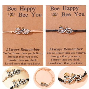 Detail of woven friendship bracelet with infinity pendant, bee charms, and Sister engraving
