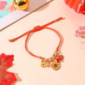 Detalle de pulsera de girasol naranja con dijes dorados y decoración de hojas de maple
