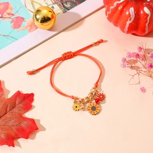 Detalle de pulsera tejida naranja con colgantes de girasol y elementos decorativos otoñales