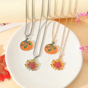 Dettaglio di ciondoli zucca e foglia d'acero smaltati su catene color oro e argento